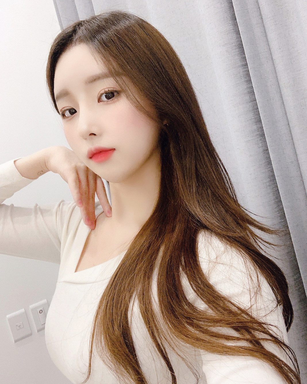 흰 커튼 앞에서 손을 턱에 대고 선 여성 셀피